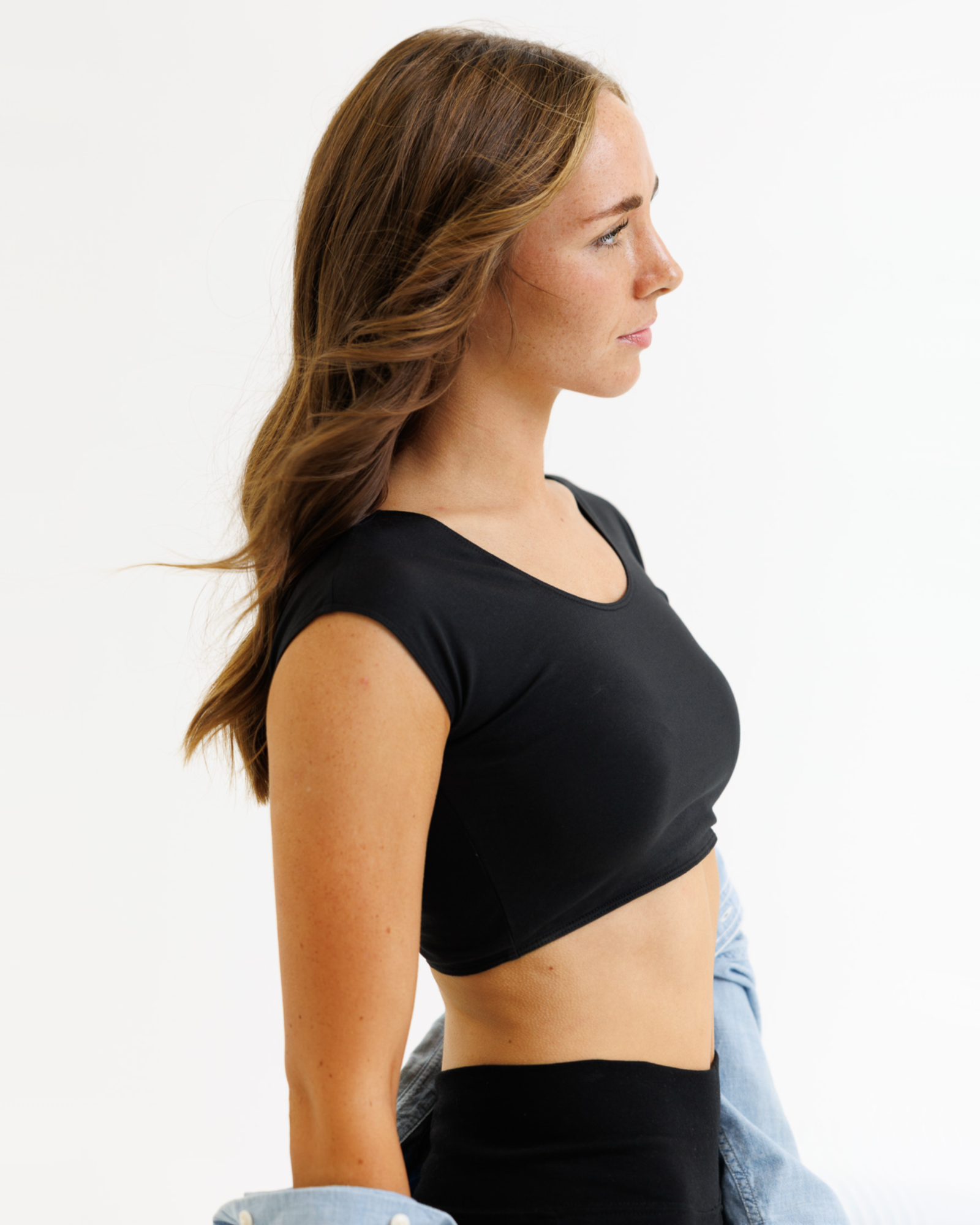 Woman wearing a black cropped layering top on a white background