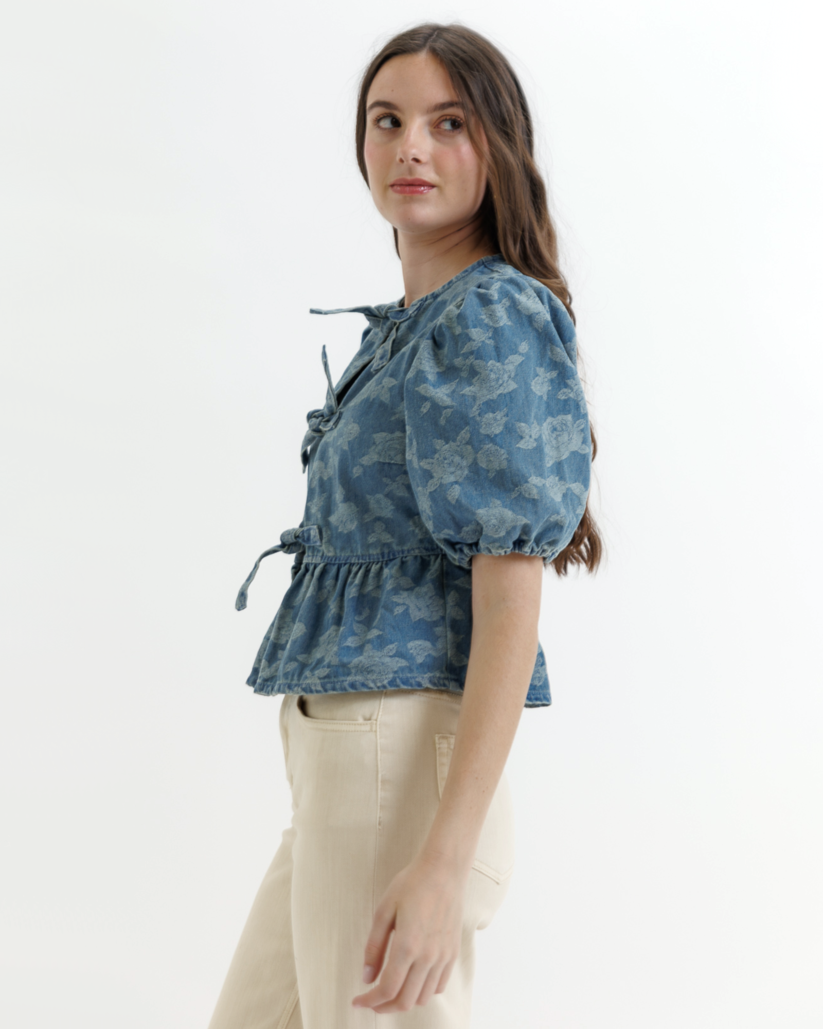 Woman wearing a blue denim floral blouse with puffed sleeves on a white background