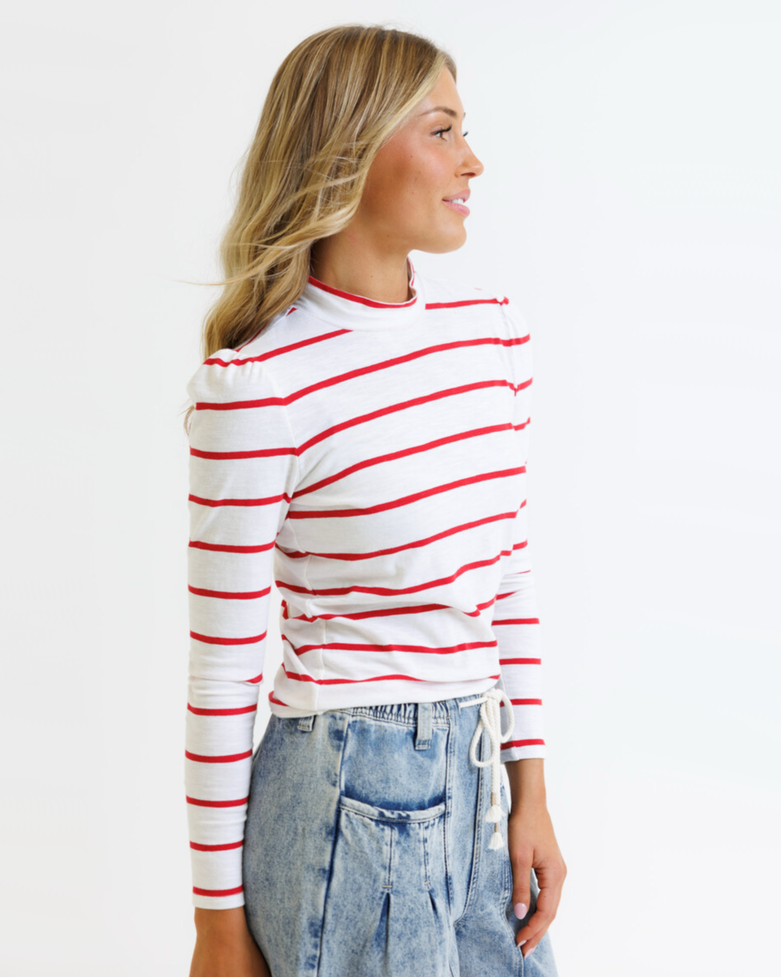 Woman wearing a white long-sleeve shirt with red stripes and blue jeans on a white background