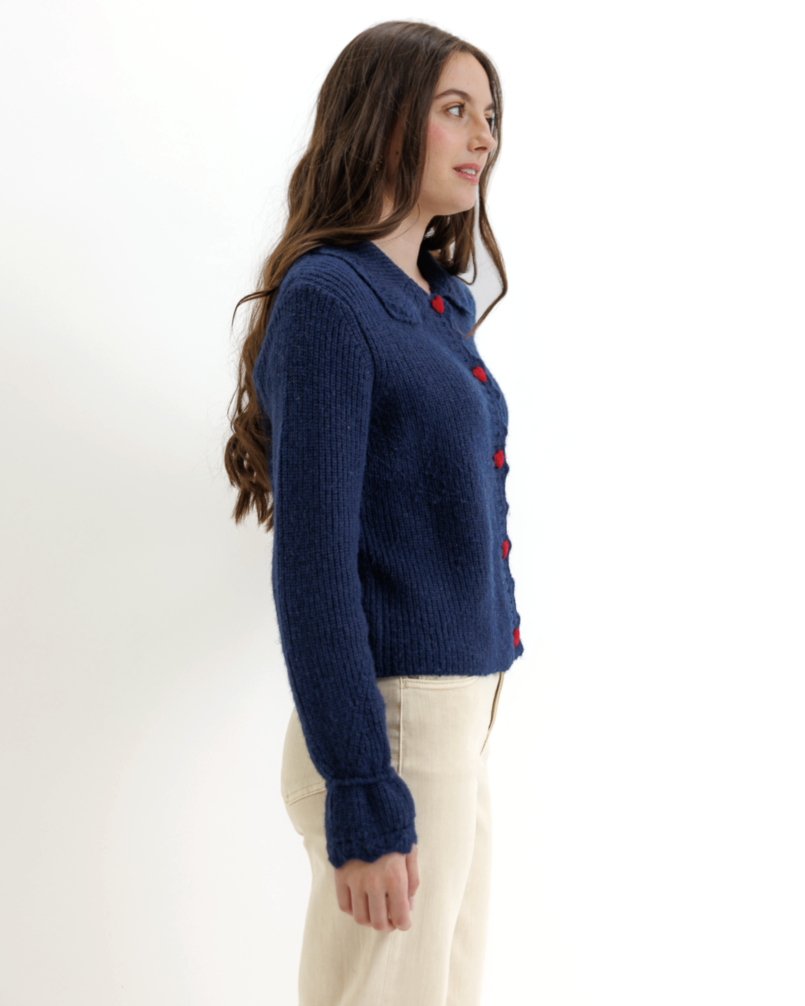 Woman wearing a blue knitted cardigan with red heart-shaped buttons on a white background