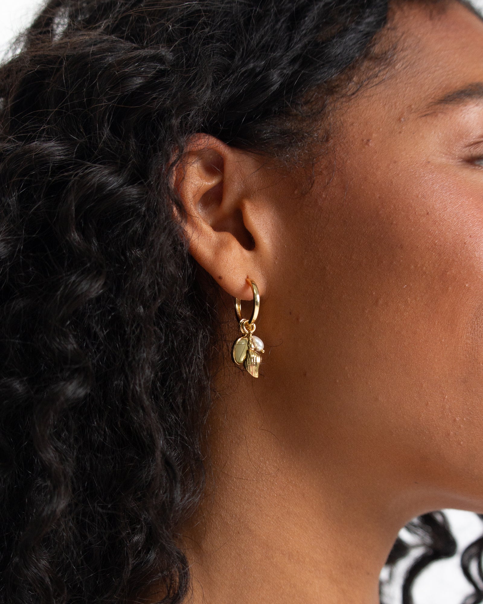 Close-up of a person wearing gold hoop earrings with leaf details.
