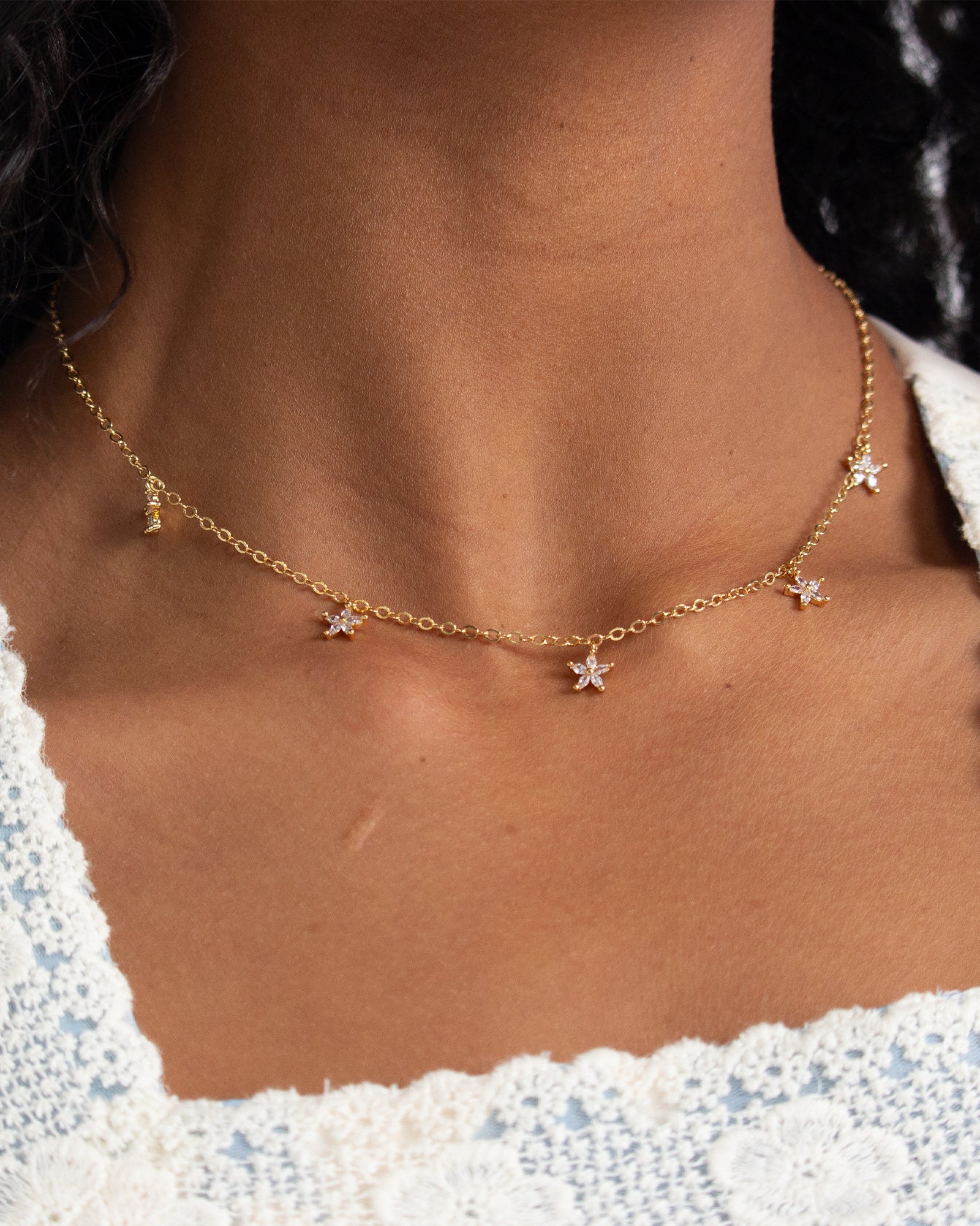 Gold necklace with star pendants on a person wearing a white top.