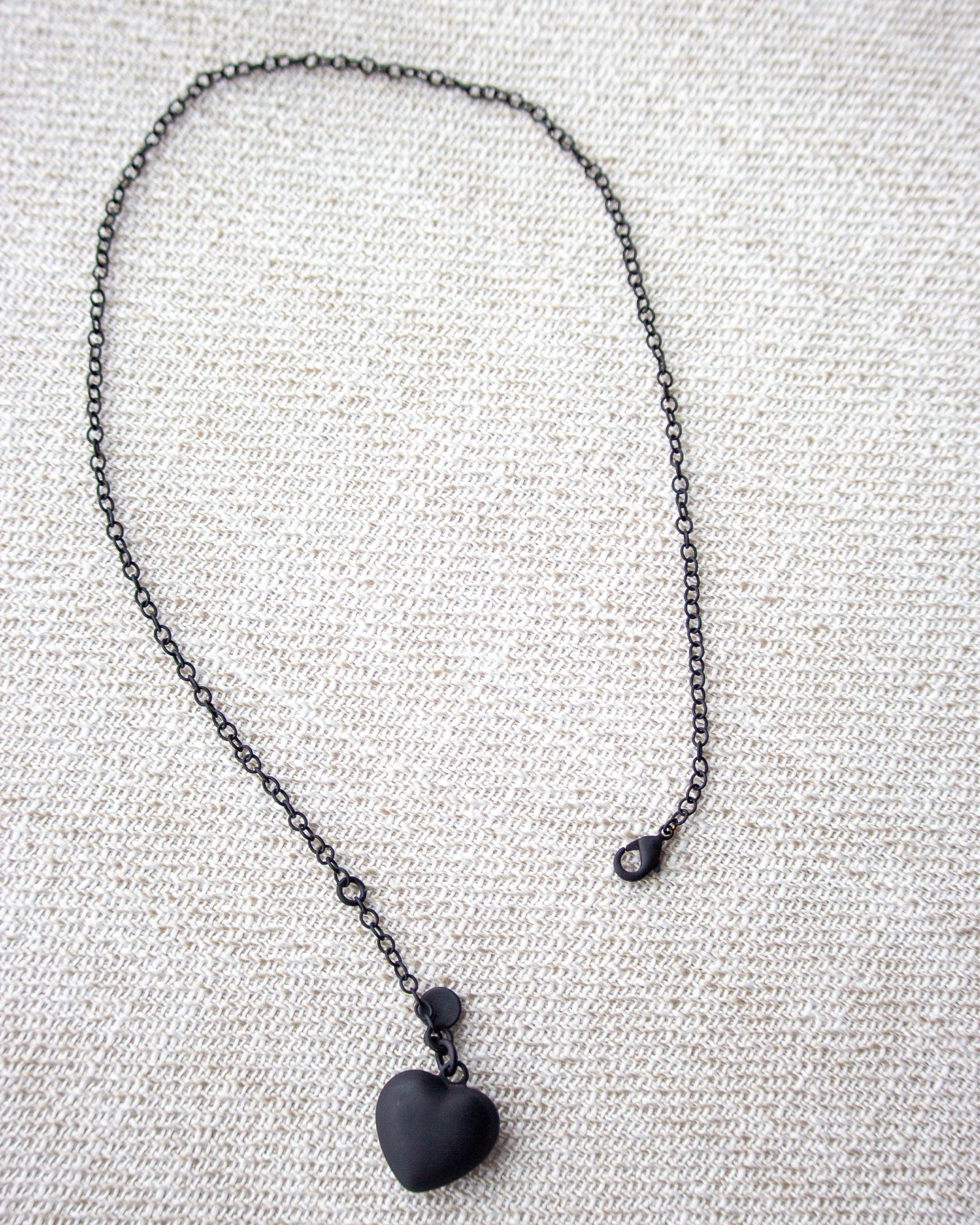 Black heart pendant necklace on a textured fabric background