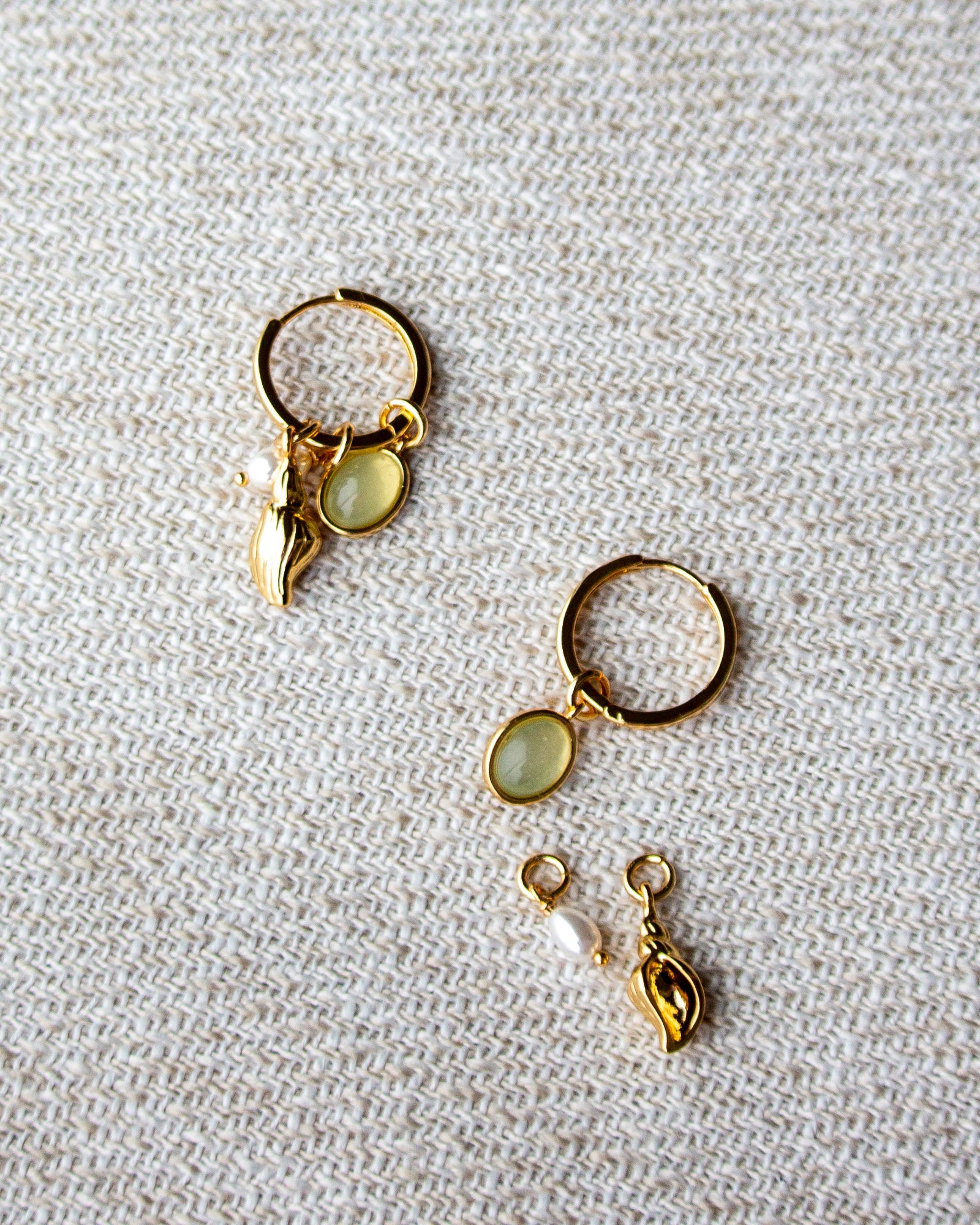 Gold hoop earrings with green gemstones on a textured beige surface