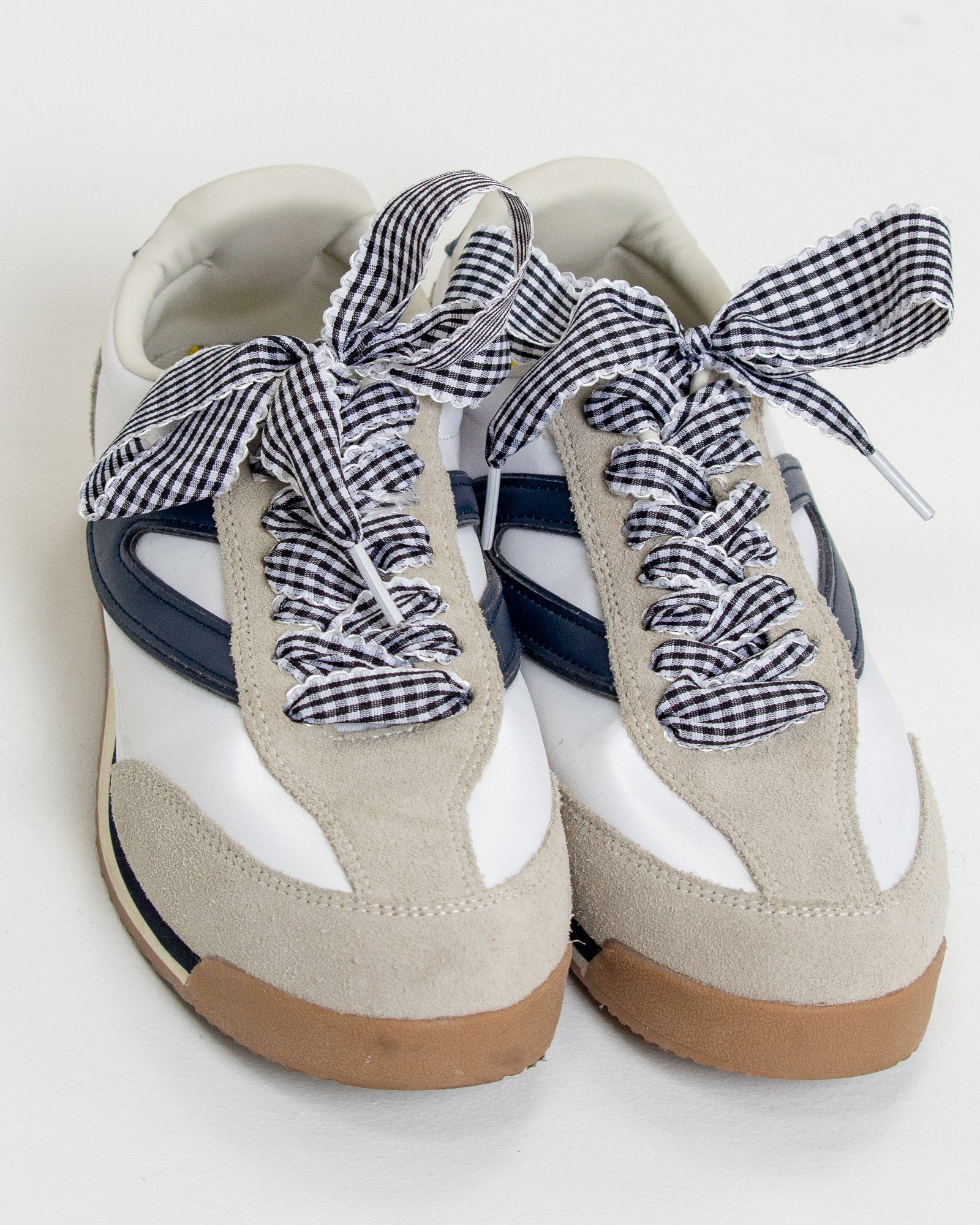 Pair of white sneakers with gingham checkered laces on a white background