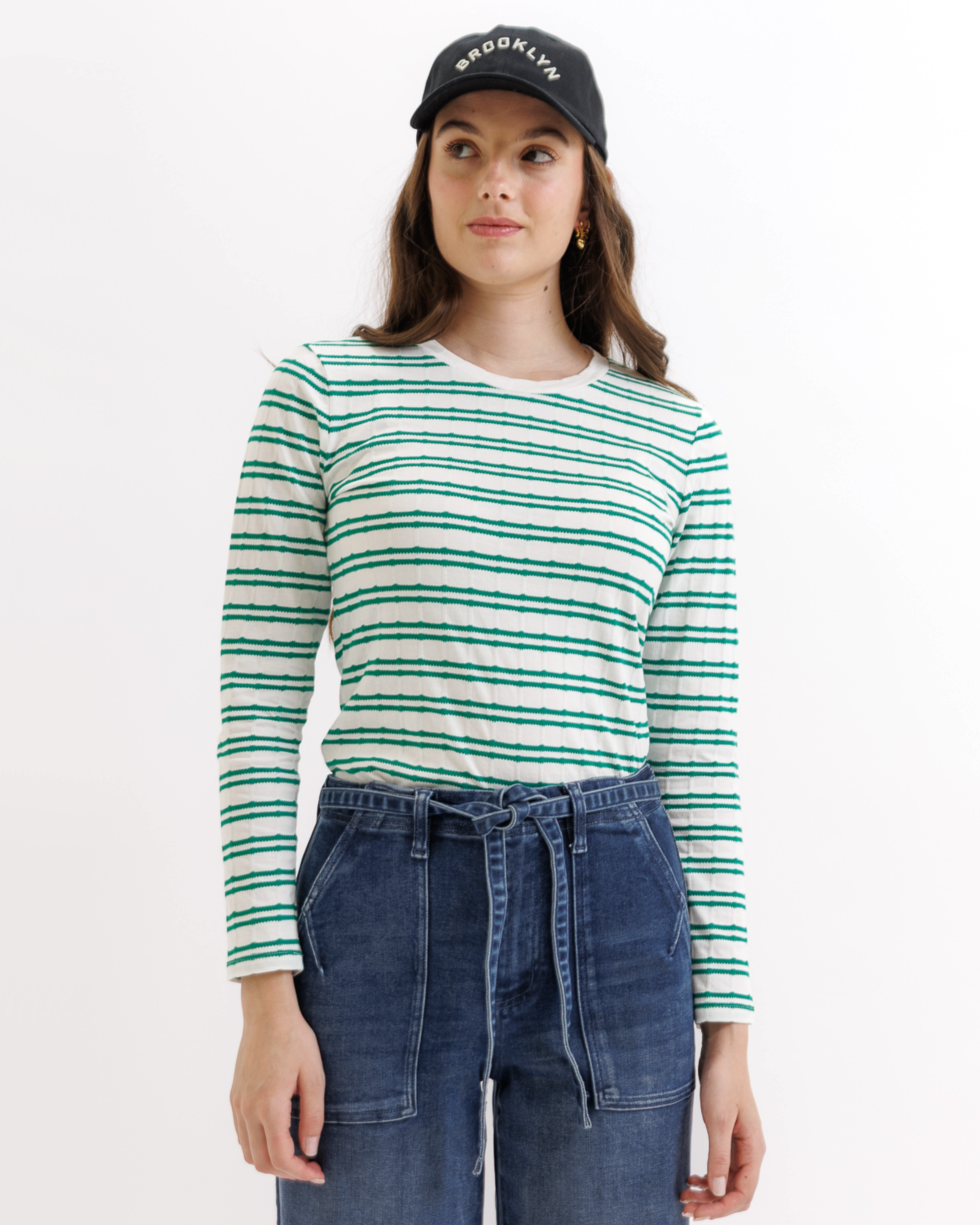 Woman wearing a green and white striped long-sleeve shirt and blue jeans on a white background