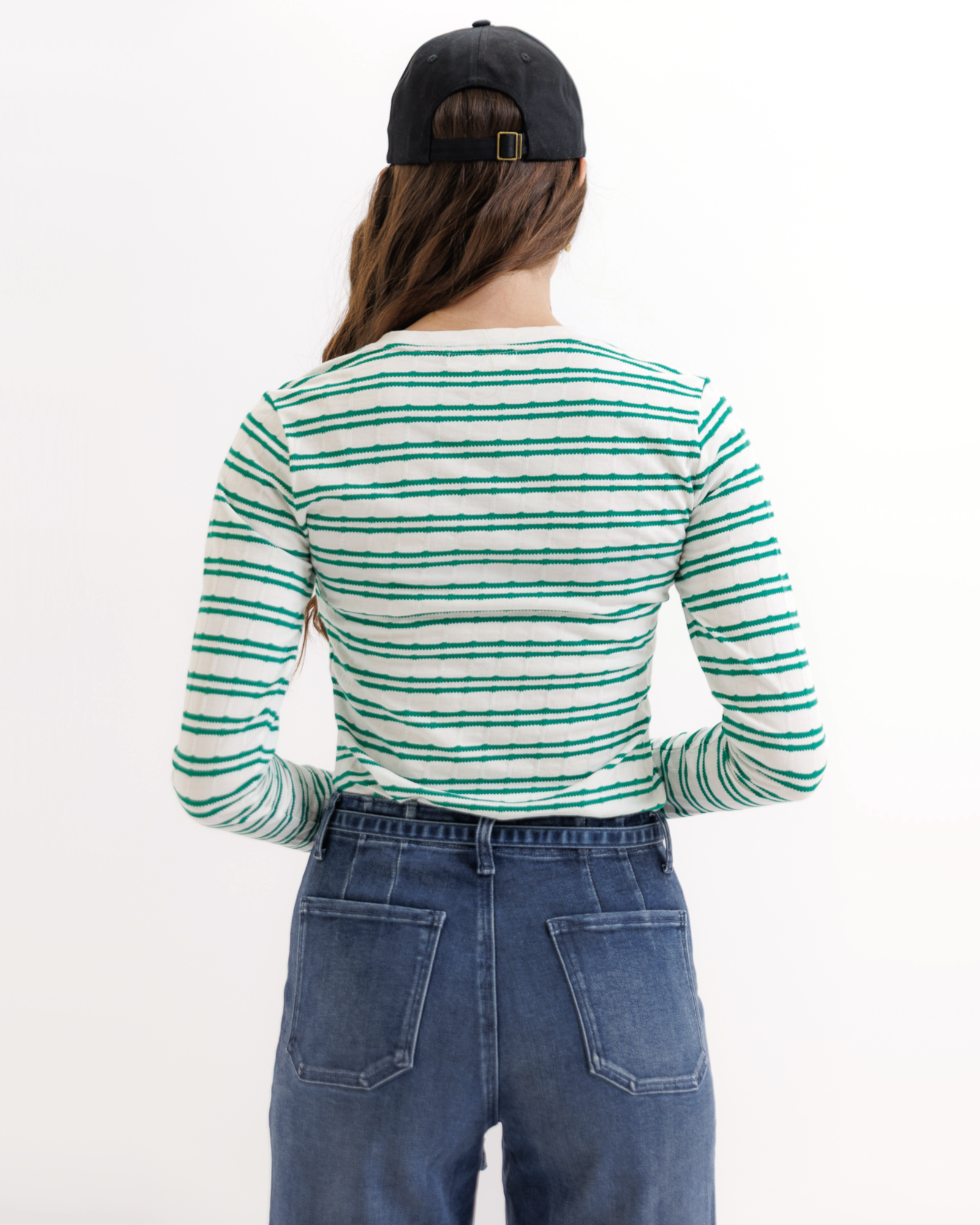 Woman wearing a green and white striped long-sleeve shirt and blue jeans on a white background