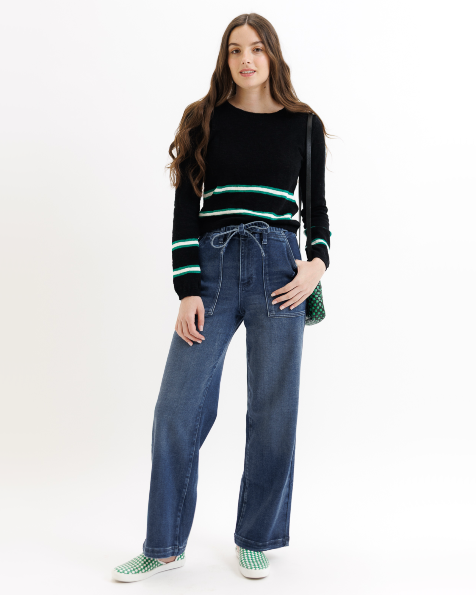 Woman wearing a black sweater with green stripes and blue jeans on a white background