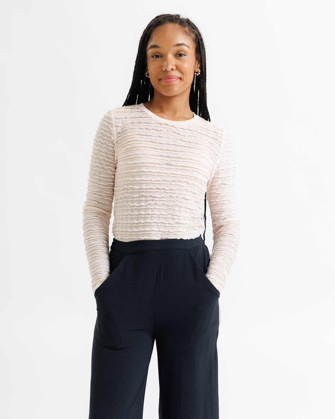 Woman wearing a cream lace top and dark wide-leg pants on a white background