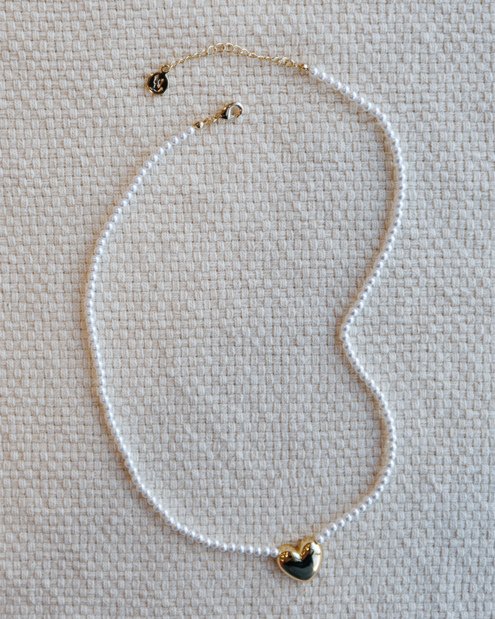 Pearl necklace with a heart-shaped pendant on a textured beige surface