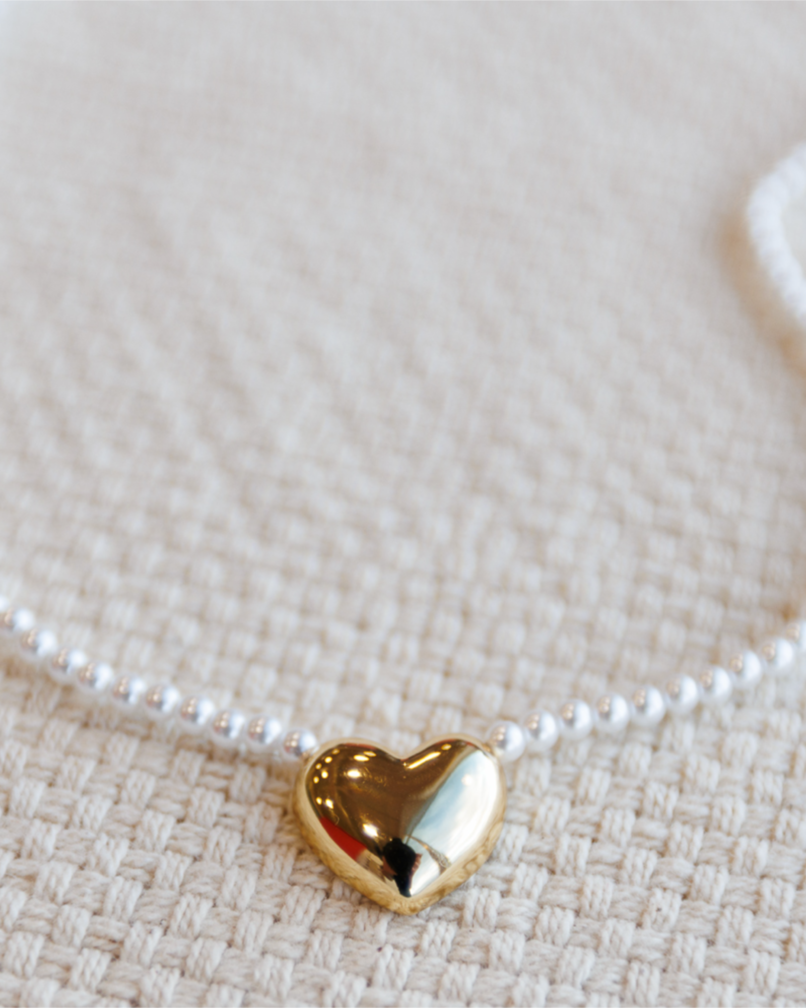 Gold heart-shaped pendant on a pearl necklace on a textured beige surface