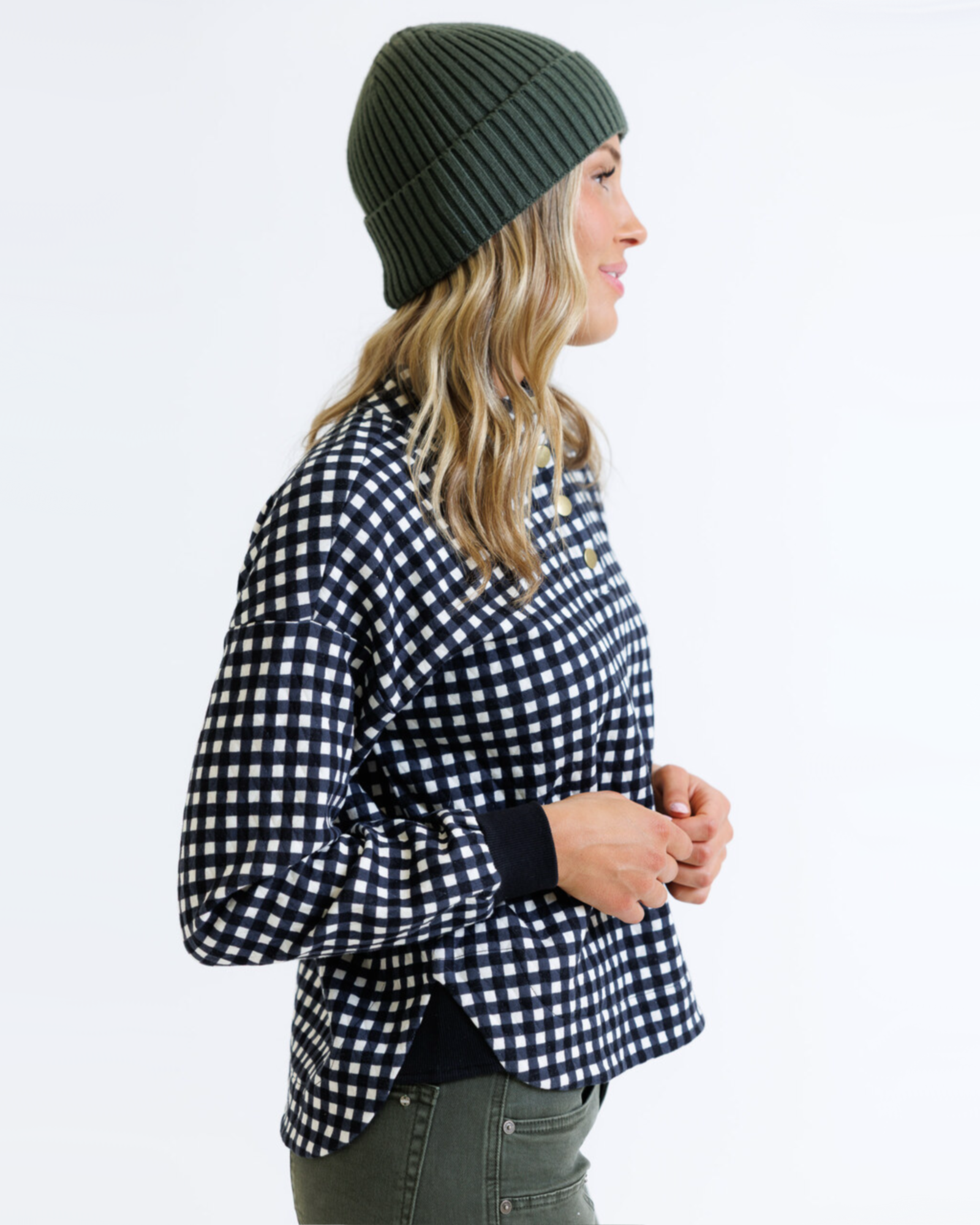 Woman wearing a black and white checkered pullover with a green beanie on a white background