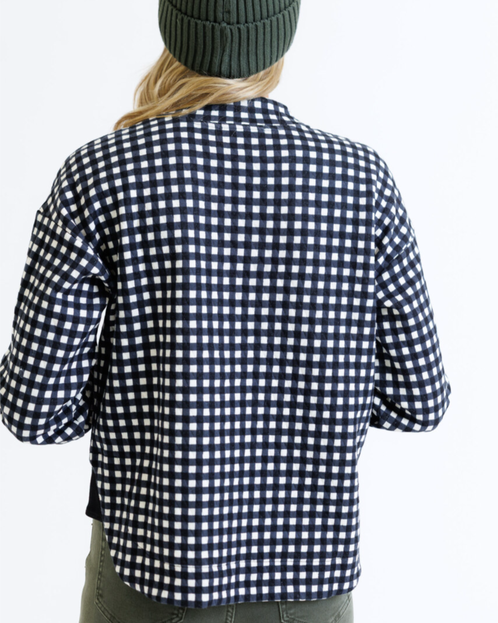 Woman wearing a black and white checkered pullover with a green beanie on a white background