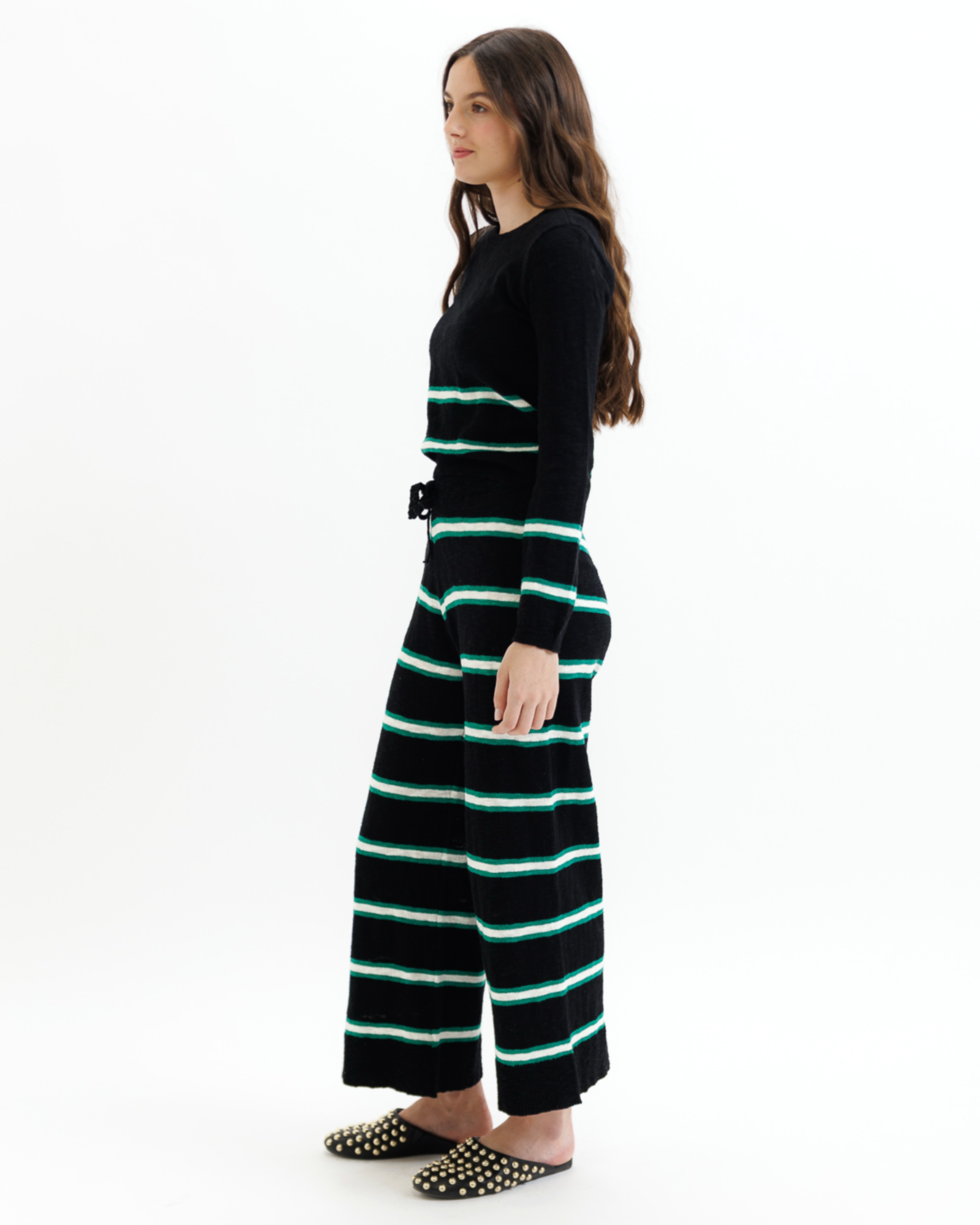 Woman wearing a black sweater and striped pants with green accents on a white background