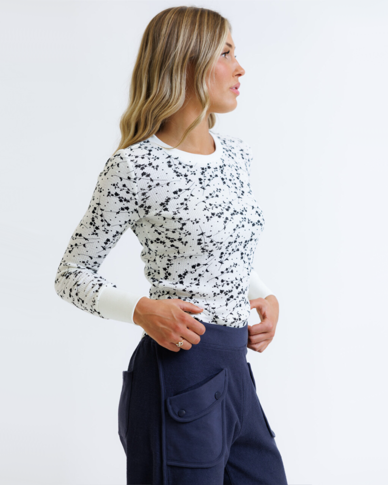 Woman wearing a white long-sleeve top with black speckles and navy pants on a white background