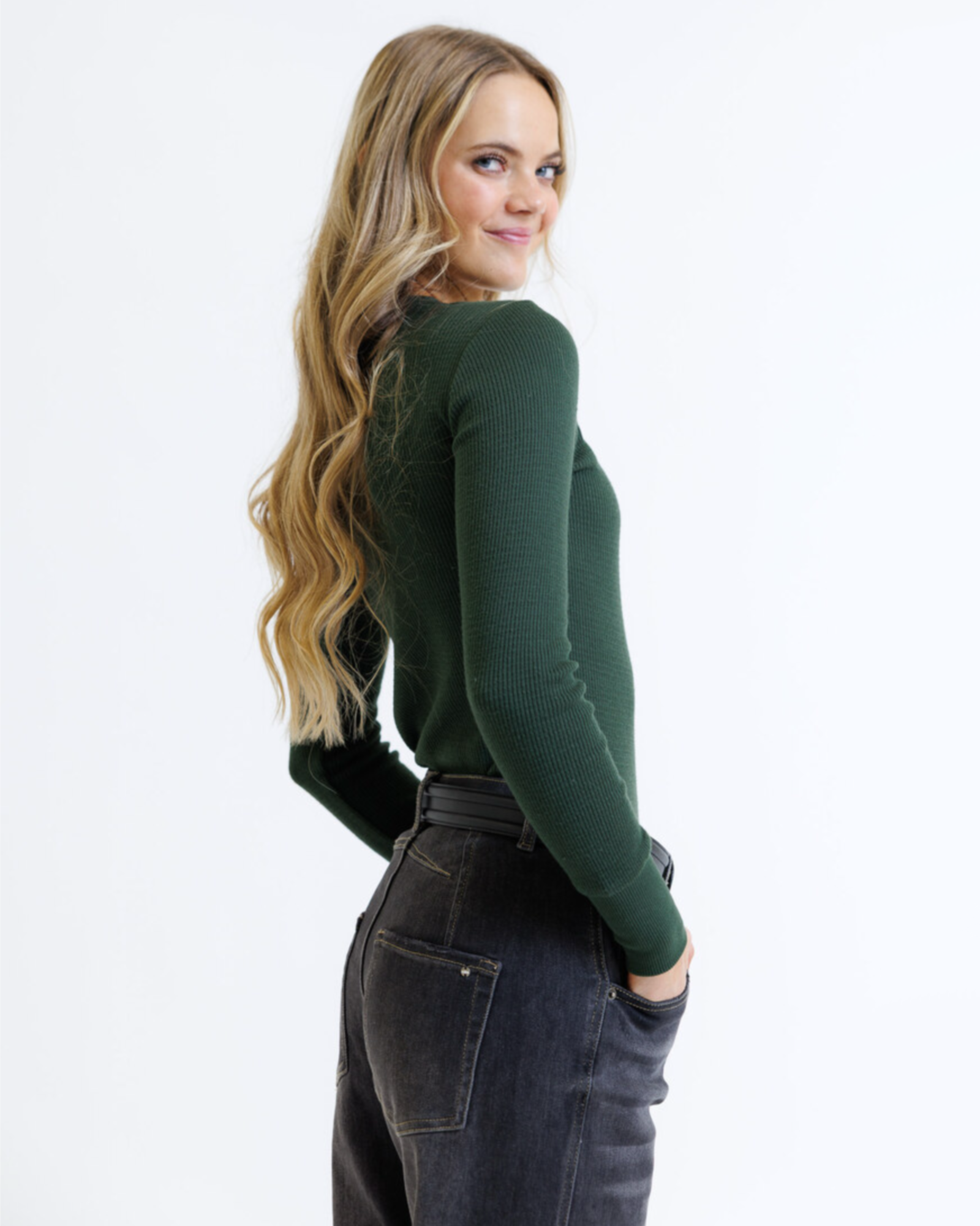 Woman wearing a green long-sleeve top and dark jeans on a white background
