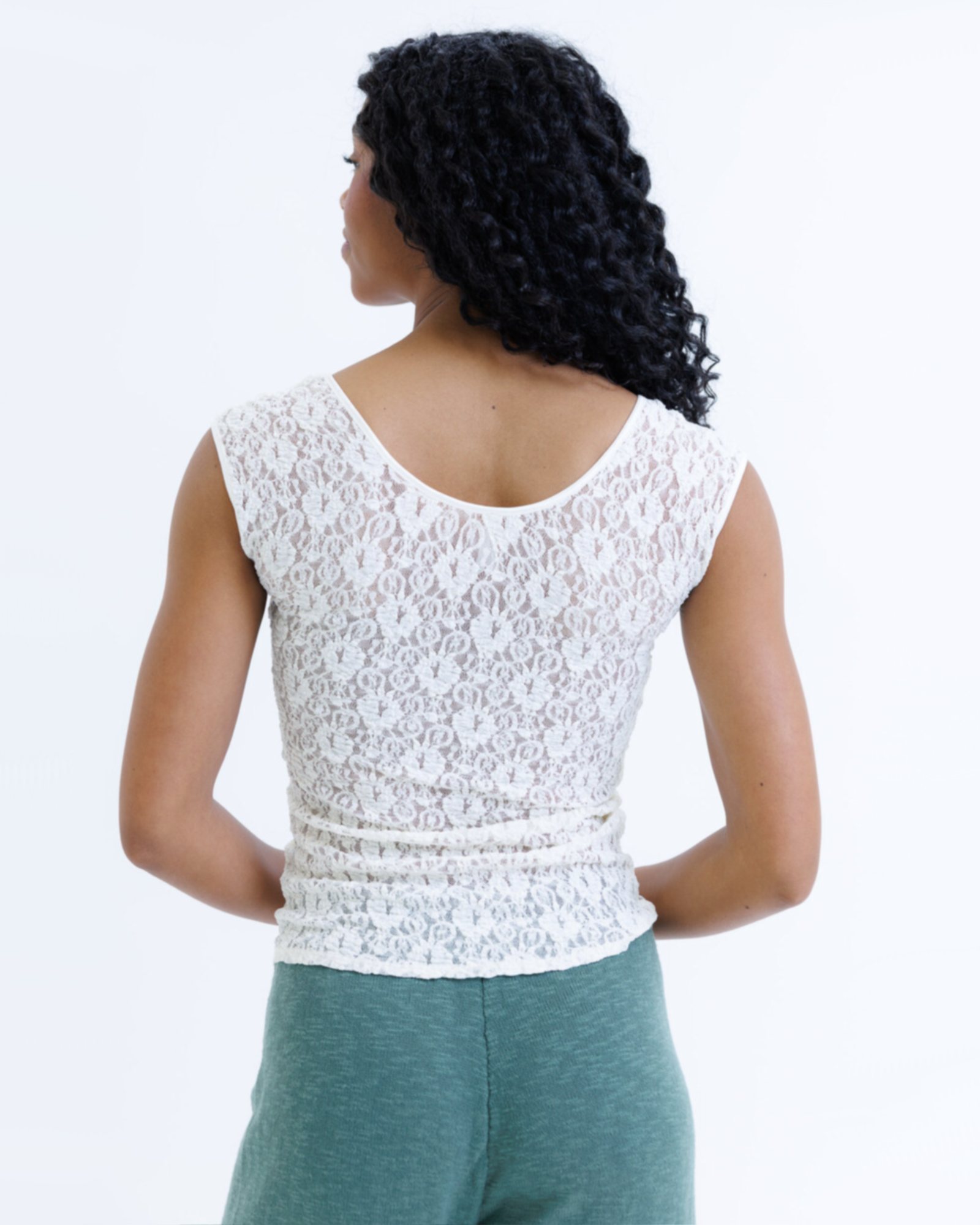 Woman wearing a white cap sleeve top and green pants on a white background