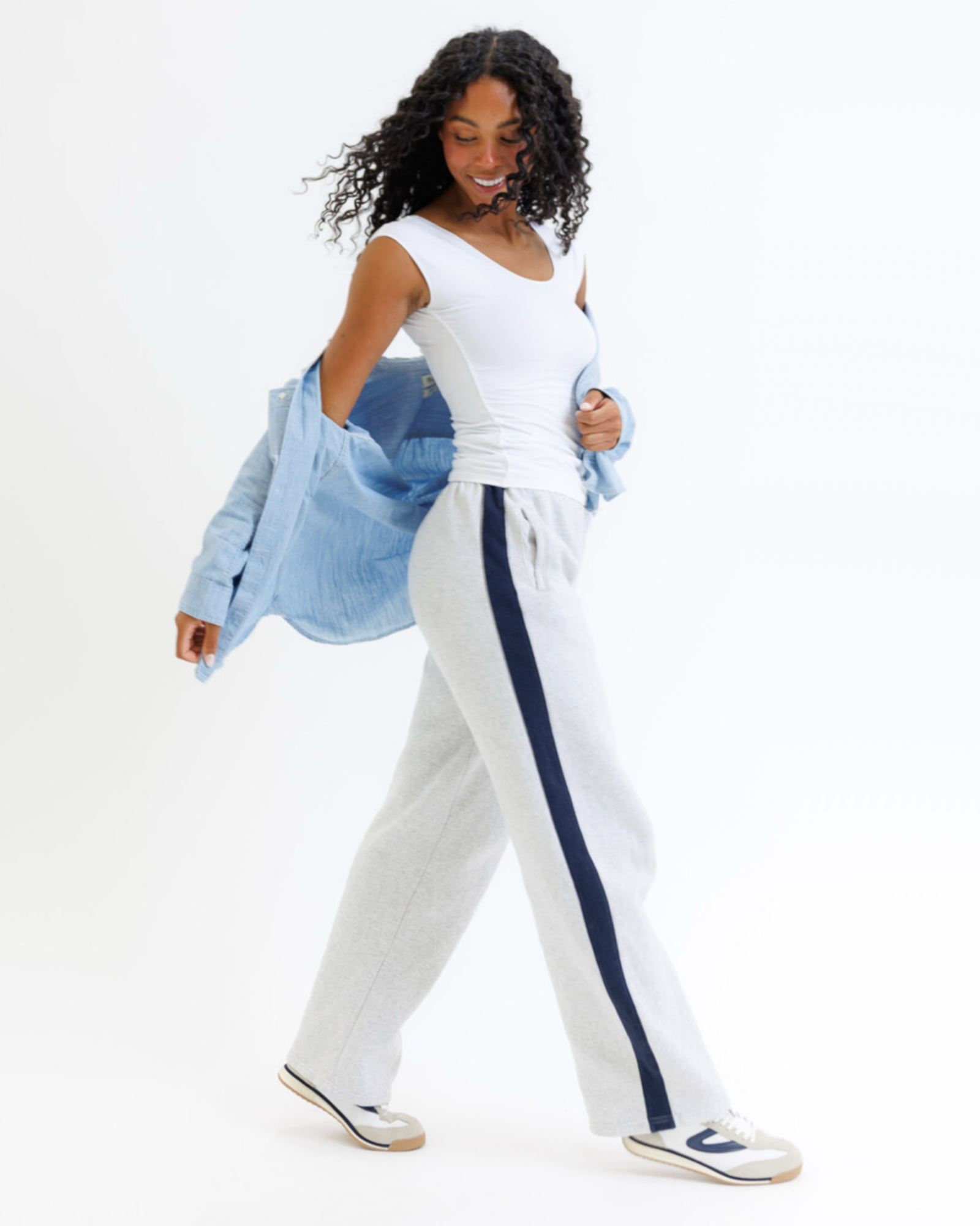 Woman wearing a white layering top and gray pants on a white background