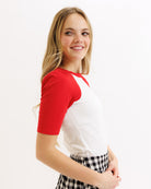 Woman wearing a red and white baseball shirt with a checkered skirt on a white background