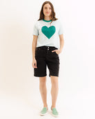 Person wearing a white t-shirt with a green heart design and black shorts on a white background