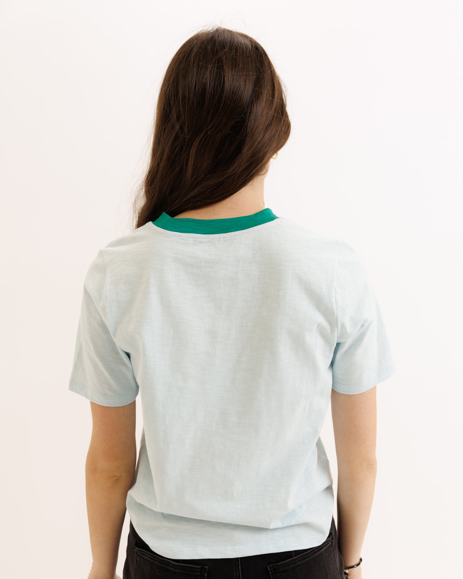 Person wearing a light gray t-shirt with green trim on a white background