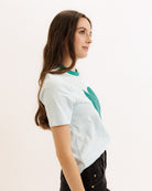 Woman wearing a white t-shirt with green accents on a plain background