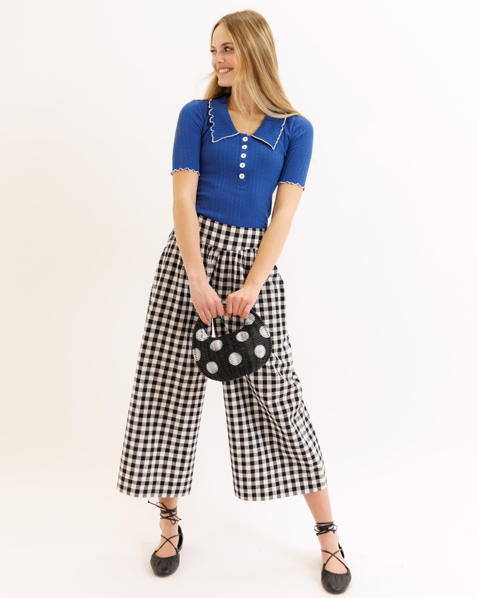 Woman wearing a blue top and black and white checkered pants holding a polka dot bag on a beige background