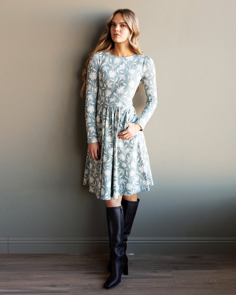 Model wearing a blue and white floral print, long sleeve, knee-length knit dress with pockets.