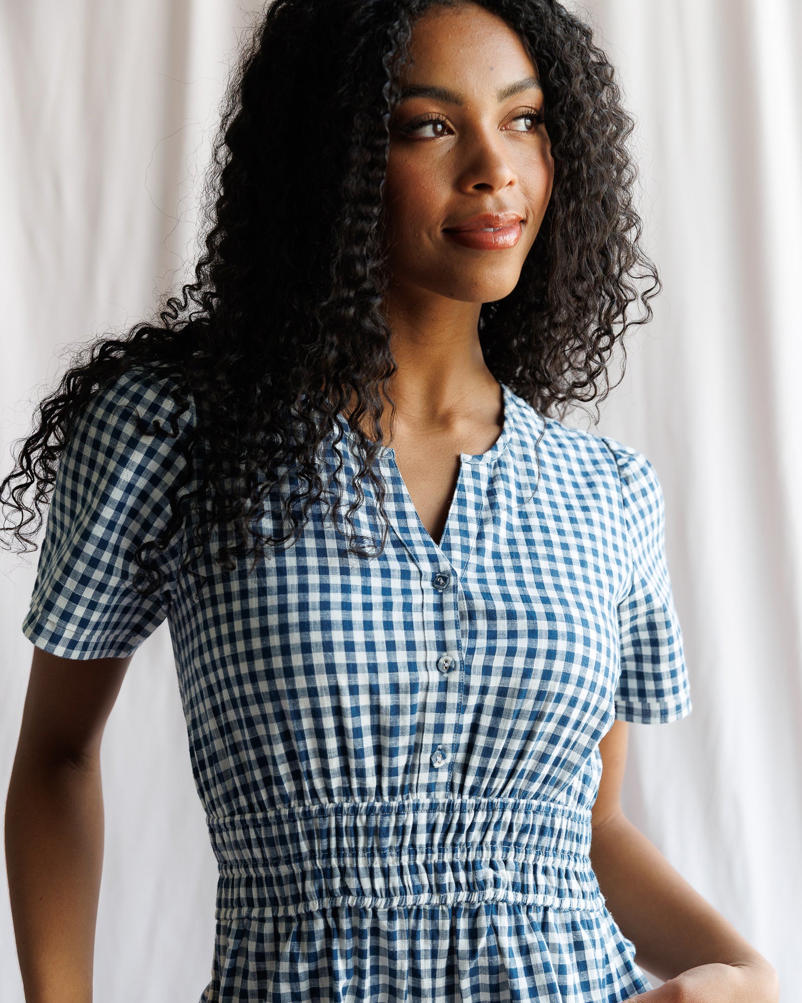 Woman wearing a blue and white checkered dress against a neutral background