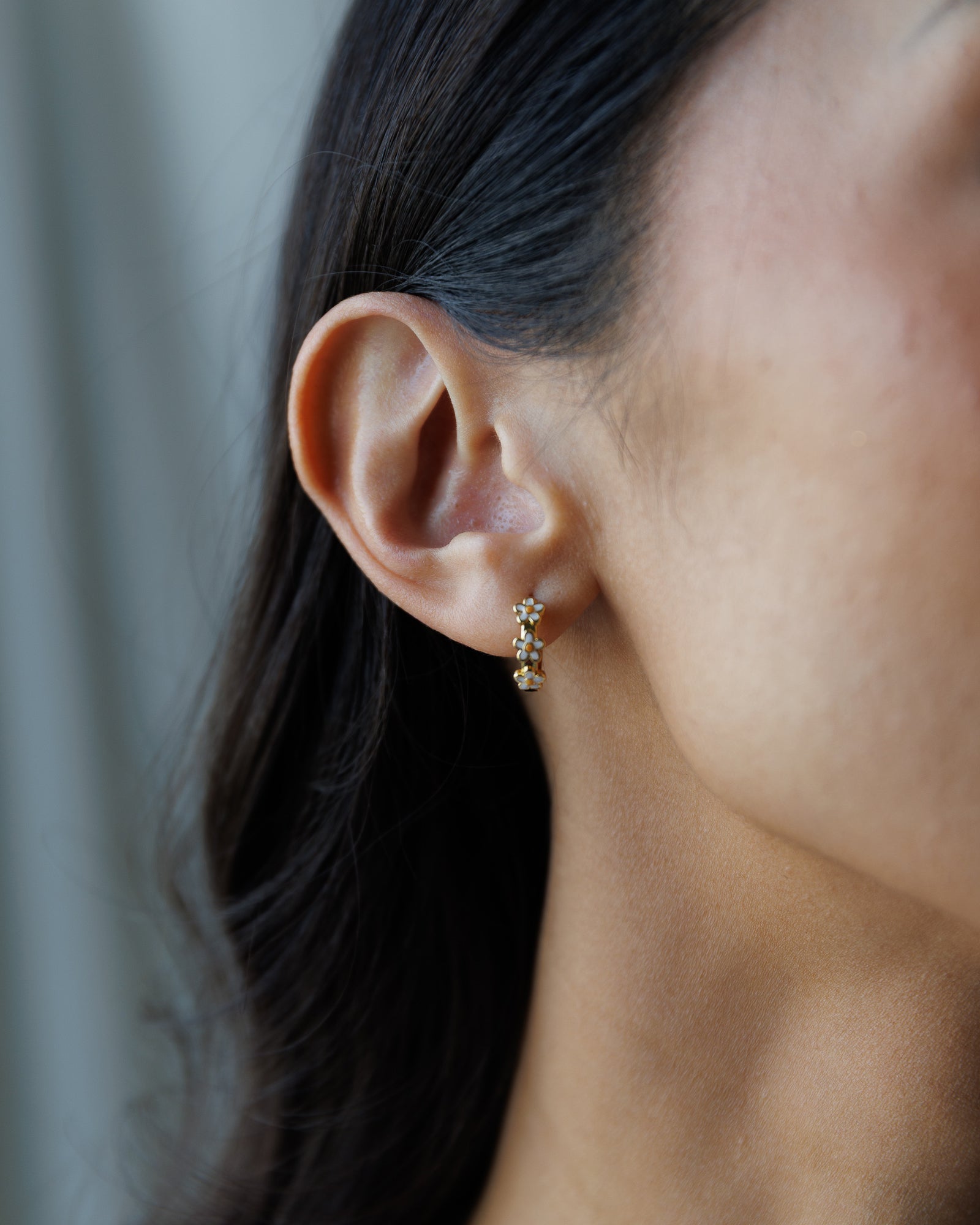 Close-up of an ear wearing a small hoop earring with a neutral background
