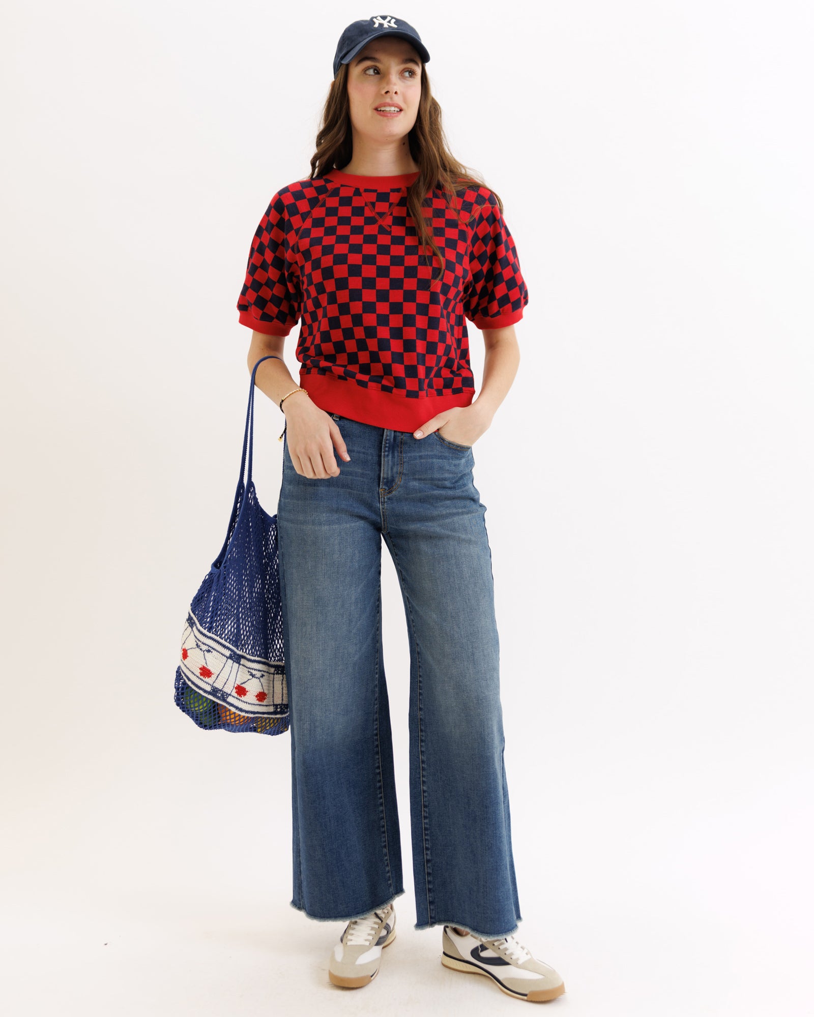 Person wearing a red and black checkered shirt, blue jeans, and a blue cap, holding a patterned bag.