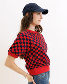 Woman wearing a red and black checkered sweater with a navy cap on a white background