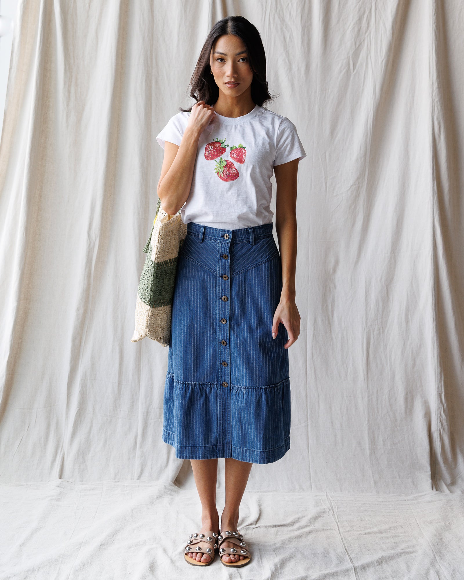 Woman wearing a white t-shirt with strawberry design and a blue skirt against a plain background