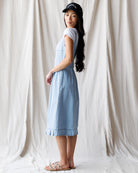 Woman wearing a light blue dress and black cap against a white curtain background