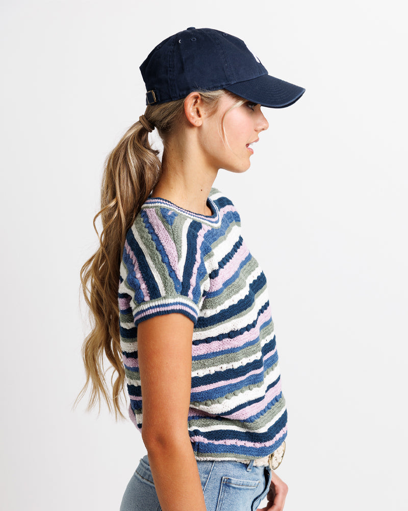 Model wearing a navy, green and purple striped short sleeve crew neck sweater