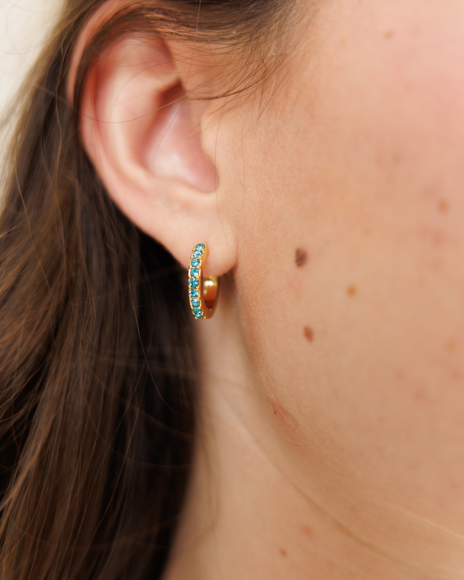 Close-up of an ear wearing a gold hoop earring with turquoise stones.