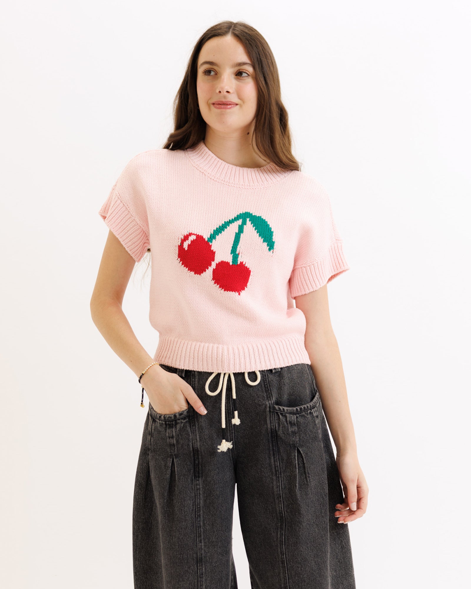 Person wearing a pink sweater with cherry design on a white background