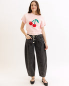 Person wearing a pink sweater with cherry design and black jeans on a white background
