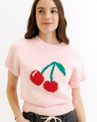 Person wearing a pink sweater with cherry design on a white background
