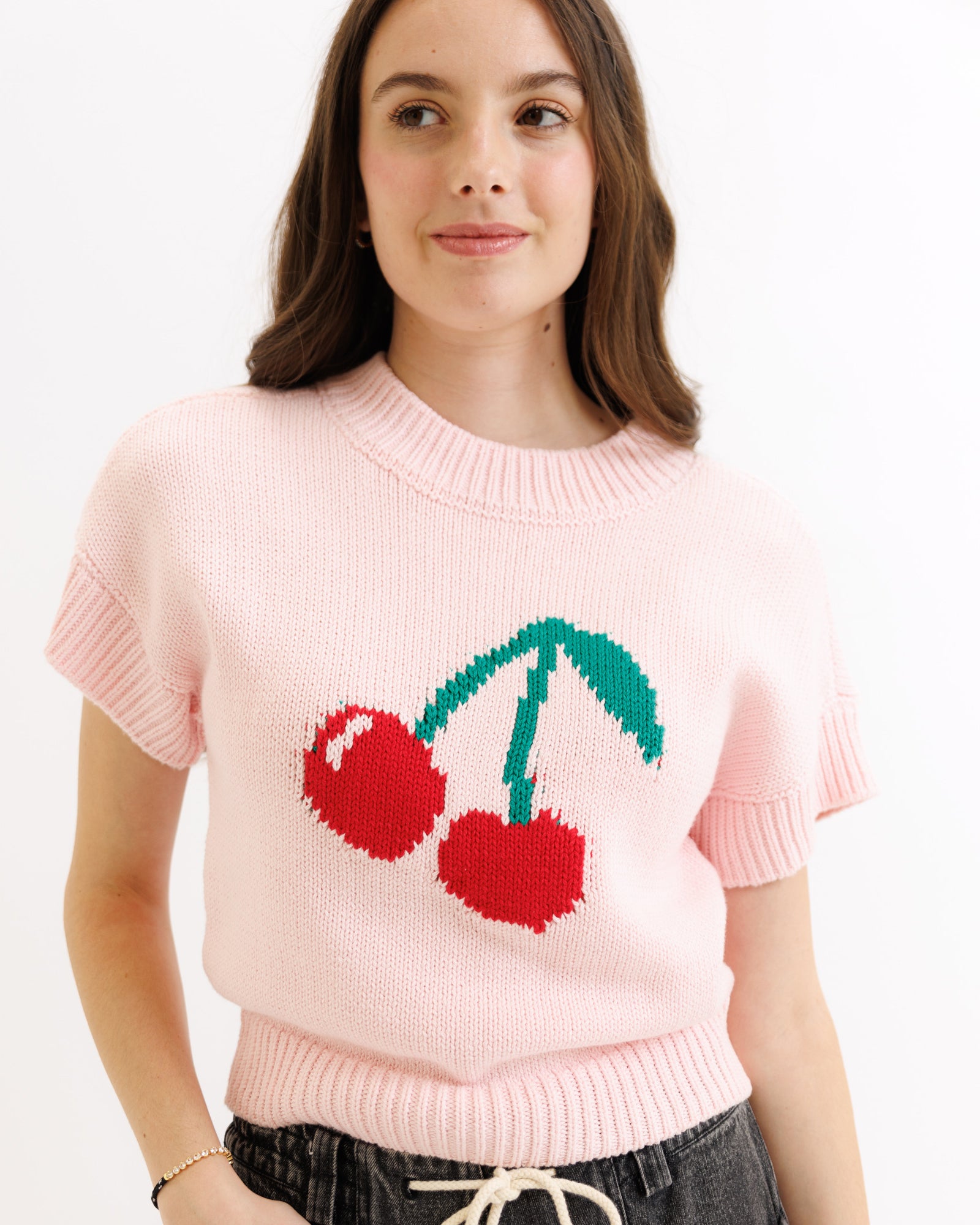 Person wearing a pink sweater with cherry design on a white background