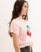 Woman wearing a pink sweater with cherry design on a plain background