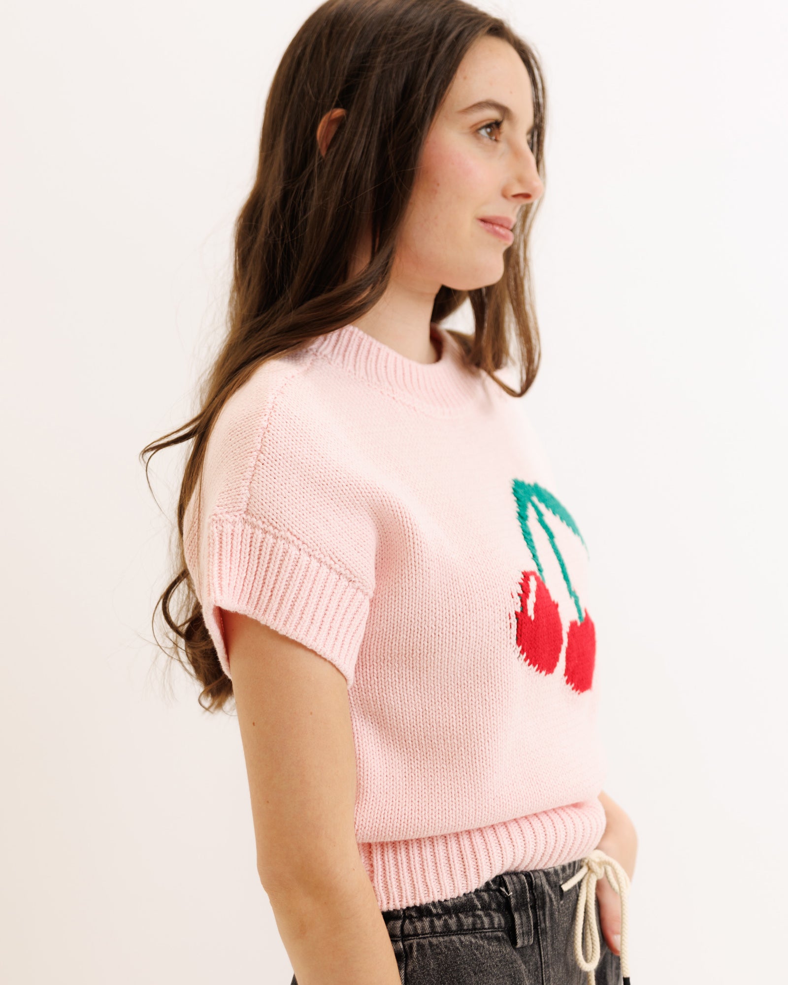 Woman wearing a pink sweater with cherry design on a plain background