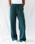 A person wearing dark teal green wide-leg sweatpants, shown from the waist down against a white fabric backdrop.