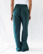 A person shown from the back wearing dark teal wide-leg pants with an elastic waistband, paired with a white top, against a white fabric backdrop.