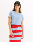 Woman wearing a light blue t-shirt and red and white striped skirt with a black cap.