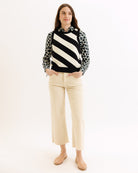 Woman wearing a black and white striped sweater with leopard print collar and beige pants on a white background