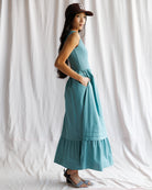 Woman wearing a teal dress and cap against a white curtain background