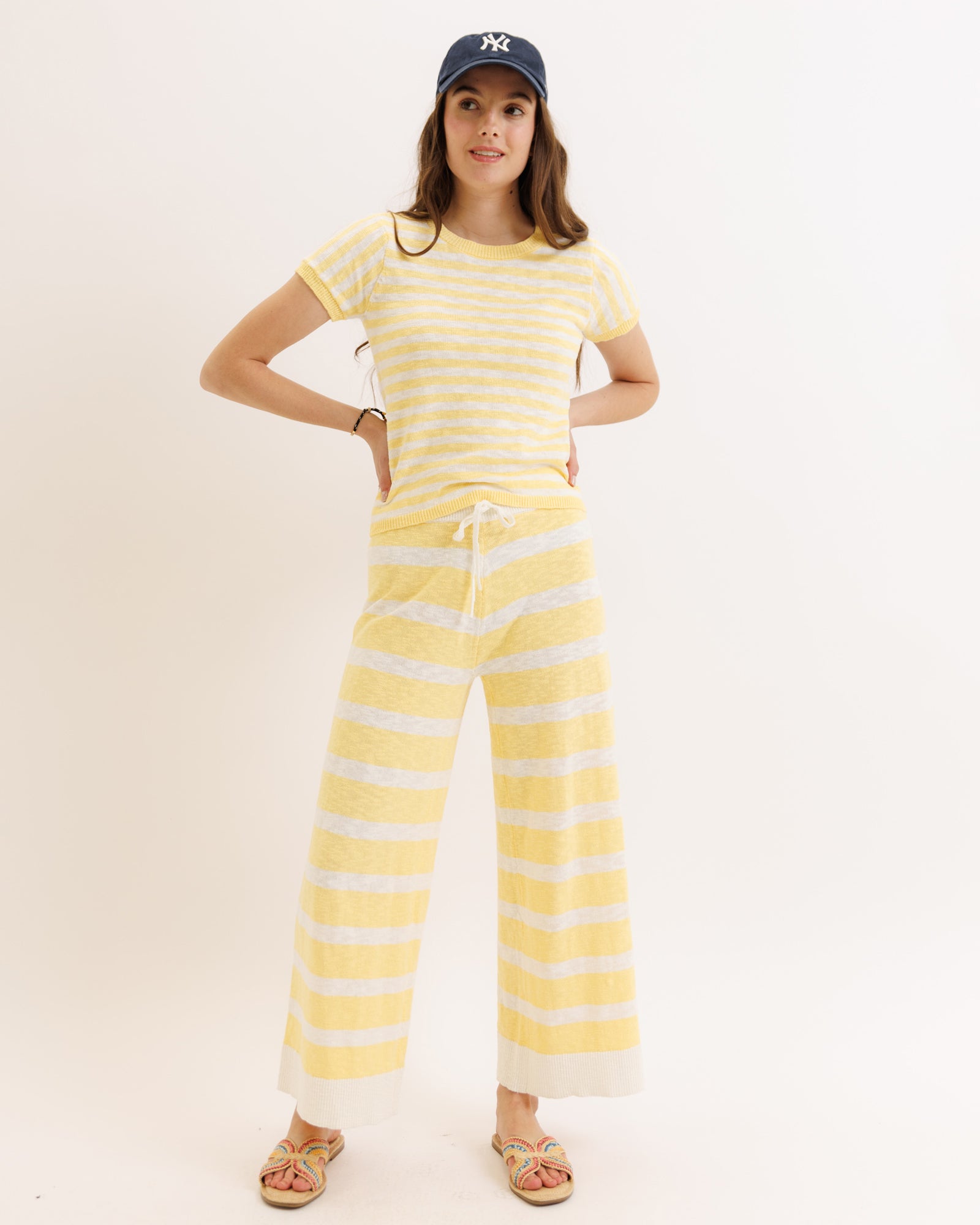 Woman wearing a yellow and white striped outfit with a cap on a plain background