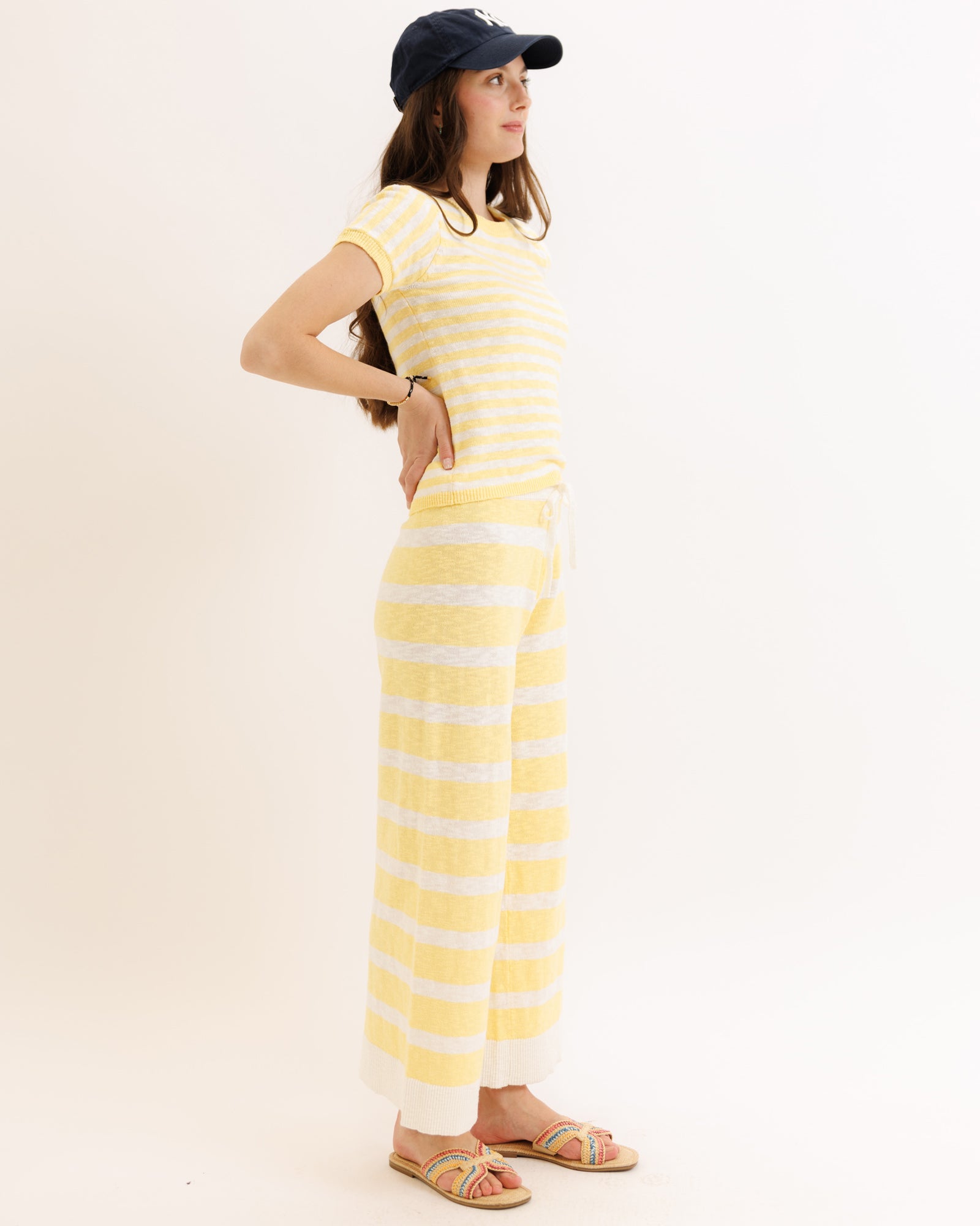 Woman wearing a yellow and white striped dress with a navy cap on a plain background
