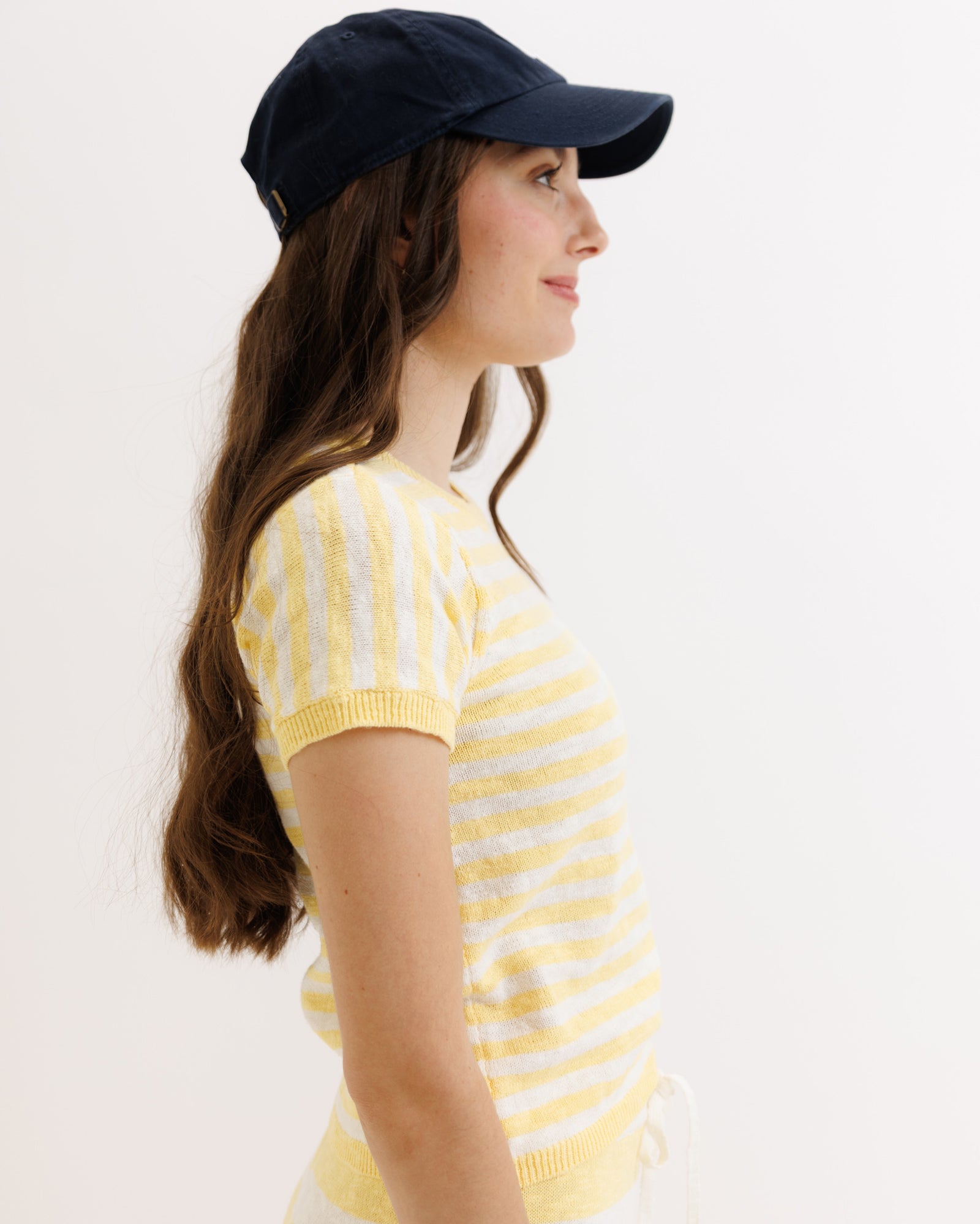 Woman wearing a yellow and white striped shirt and navy cap on a plain background